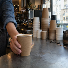 Gobelet carton kraft rempli de café sur le comptoir d'un coffee shop, piles de gobelets blancs et kraft
